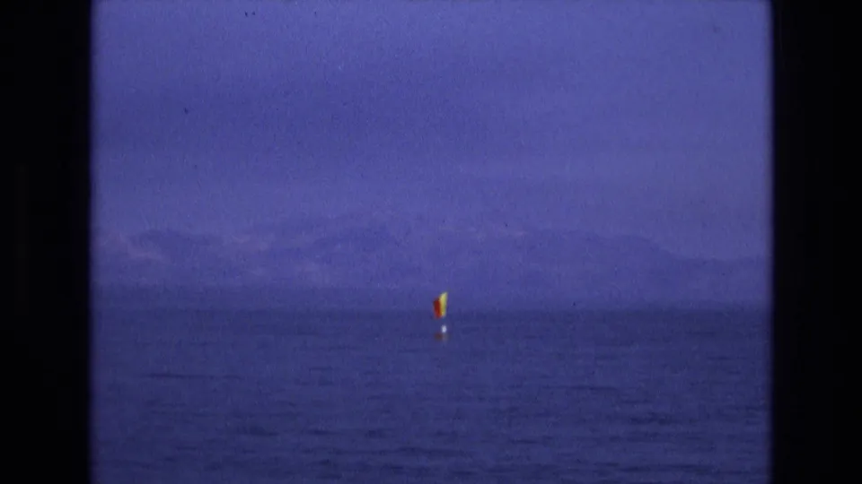 Final frame of the 1973 8mm Salt Lake City, Utah clip shows a small yellow sailboat on open water, distant mountain silhouettes, and the purple-blue color cast of aged home-movie film.