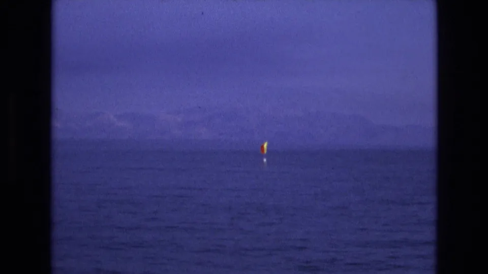Soft 8mm frame from 1973 Salt Lake City, Utah metadata showing a small red and yellow water marker with blue water, haze, and distant landforms.