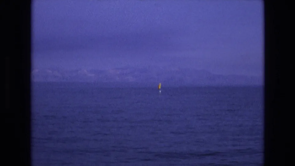 Final 1973 Salt Lake City, Utah home-movie frame with a distant red and yellow flag marker on calm water, faint mountains, and dark 8mm frame borders.