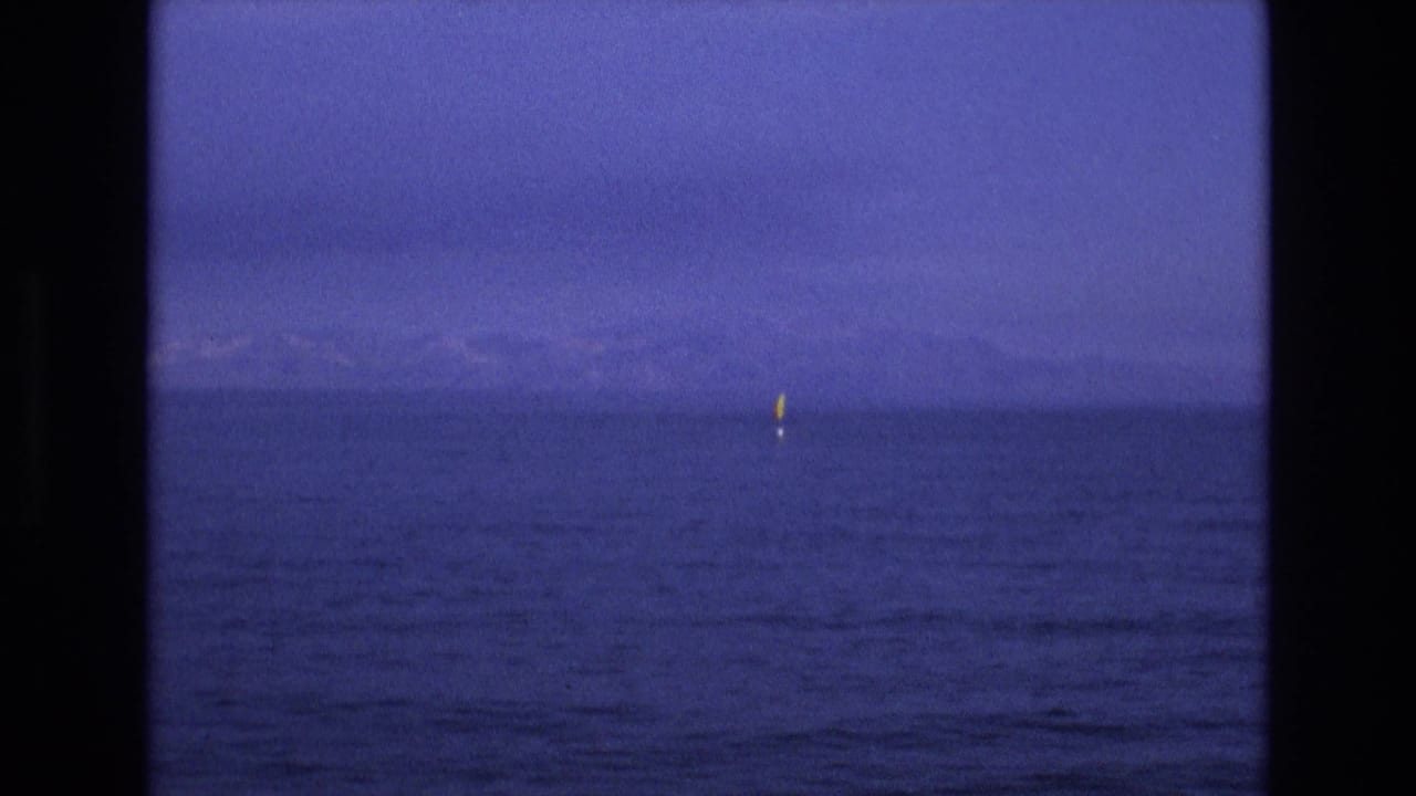 Dark-framed view of calm blue water with a low horizon and a small yellow marker.