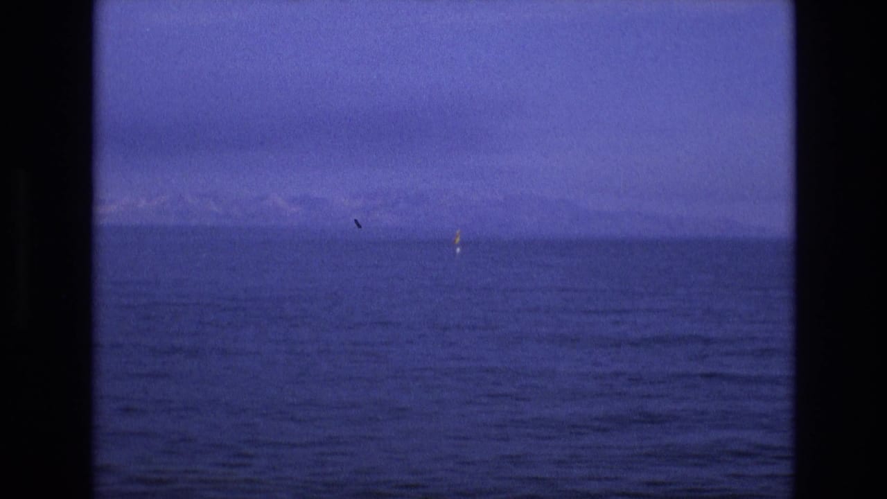 1973 8mm home-movie frame from the supplied Salt Lake City, Utah metadata showing open blue water, faint mountain or shoreline shapes on the horizon, and a small yellow marker near the right side.