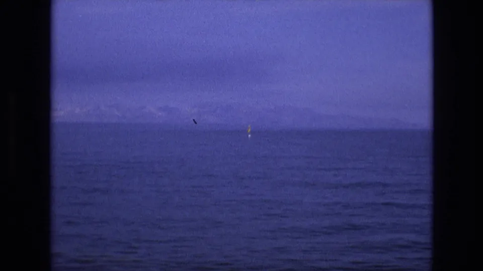 1973 8mm home-movie frame from the supplied Salt Lake City, Utah metadata showing open blue water, faint mountain or shoreline shapes on the horizon, and a small yellow marker near the right side.