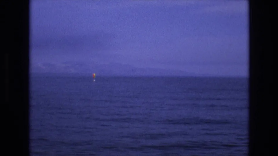1973 8mm home-movie frame from the supplied Salt Lake City, Utah metadata showing a hazy blue water horizon with a small yellow buoy-like marker and dark framing at the edges.