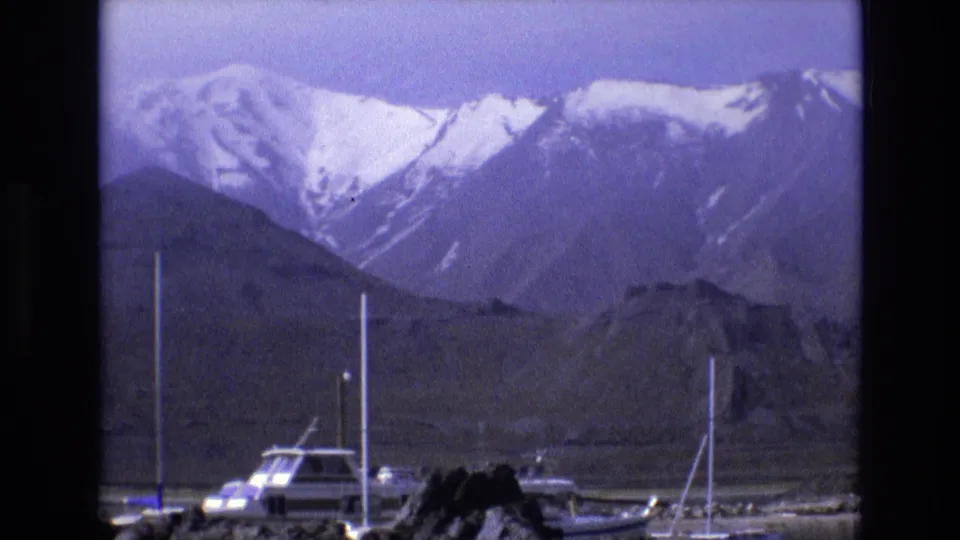 Docked boats and masts sit in the lower frame beneath broad snow-capped mountains, continuing the 1973 Utah scenic marina view.
