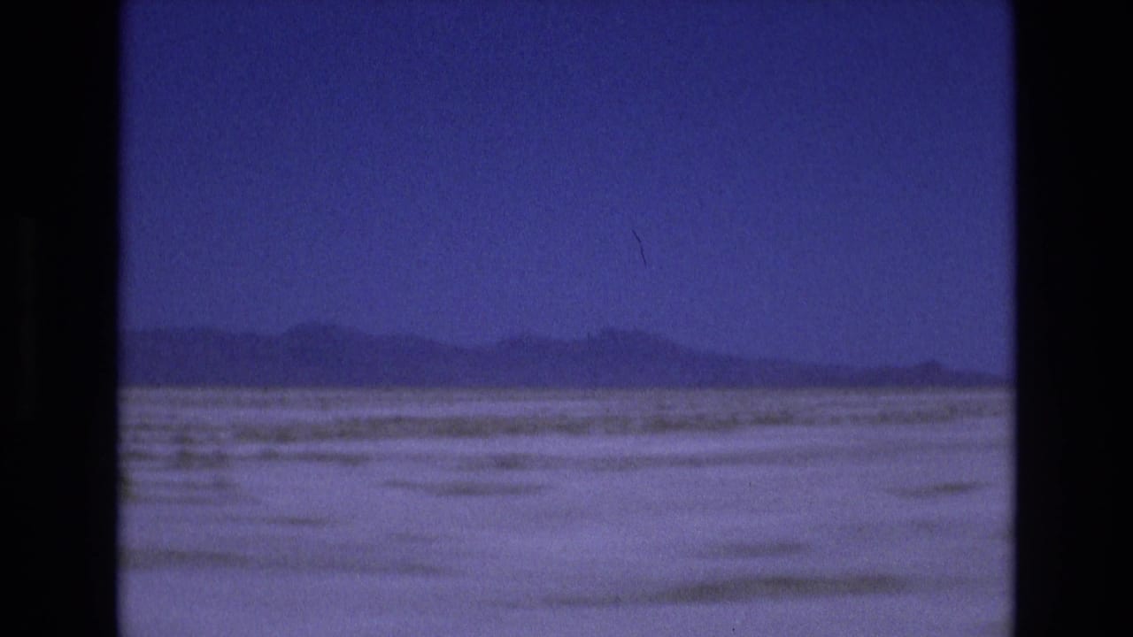 Wide pale salt-flat landscape with distant low mountains under a blue-purple sky.