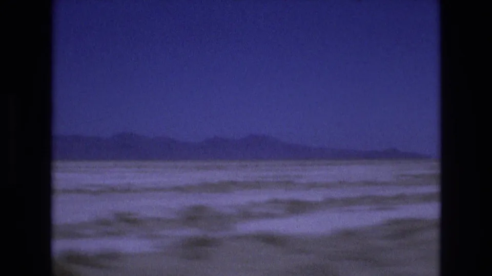 1973 Utah home-movie frame looking across a flat salt landscape toward low distant hills, with soft grain and blue-purple color shift.