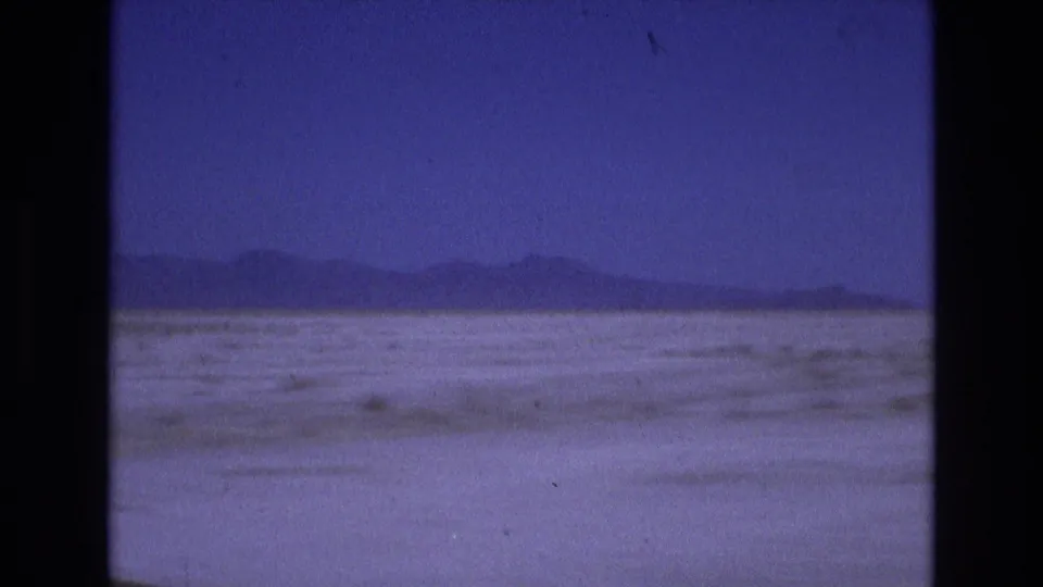 1973 Salt Lake City area travel footage frame showing a wide pale basin, a low horizon of mountains, and handheld 8mm softness.