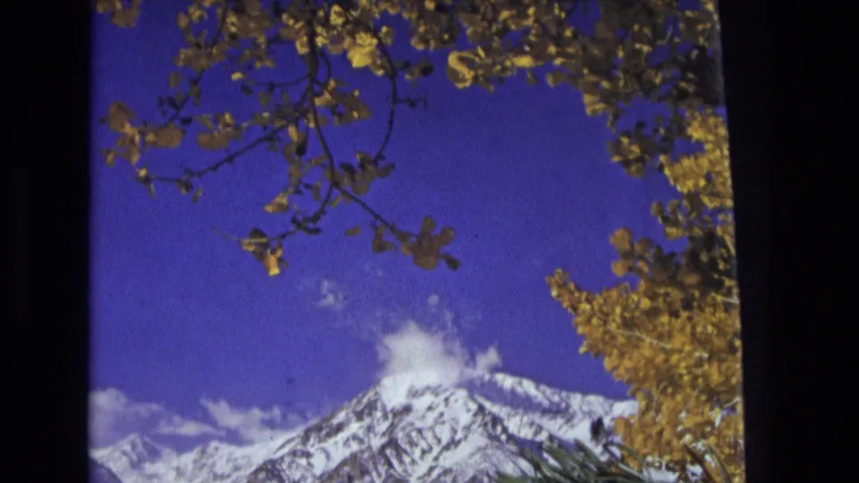 1973 Salt Lake City-area mountain view on 8mm film, with snowy ridges, deep blue sky, and yellow autumn foliage framing the shot.