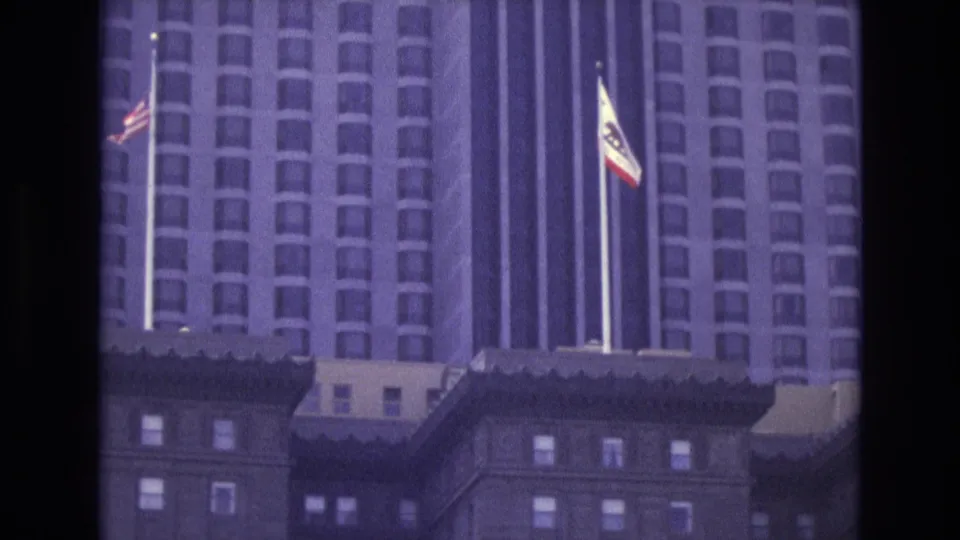 Purple-tinted 8mm view of a San Francisco high-rise with flags and older foreground architecture below.