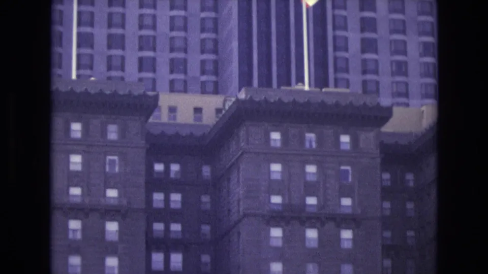 Final 1973 San Francisco 8mm frame centered on a California flag, high-rise windows, and darker foreground buildings.
