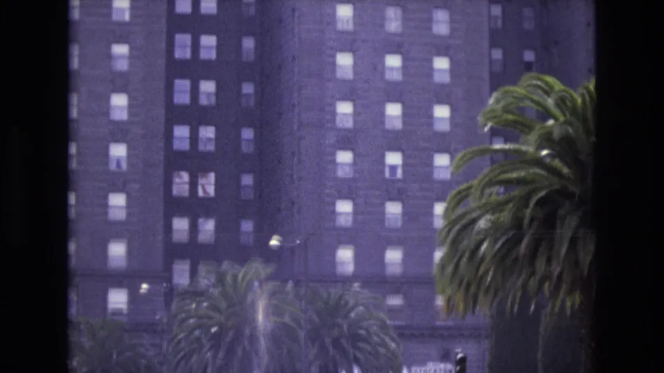 1973 San Francisco 8mm frame showing the hotel exterior with multiple palm trees in the foreground and street-level detail at the bottom of the frame.