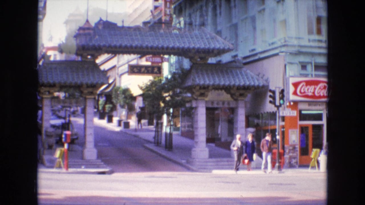 Chinatown gate over a San Francisco street with pedestrians, storefronts, and traffic signals.