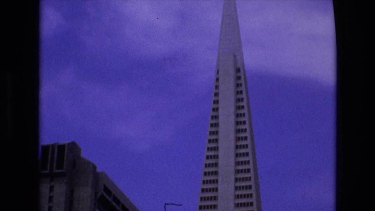 1973 San Francisco 8mm frame showing the Transamerica Pyramid from a low angle with a neighboring high-rise and dark film border visible.