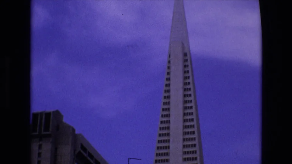 1973 San Francisco 8mm frame showing the Transamerica Pyramid from a low angle with a neighboring high-rise and dark film border visible.