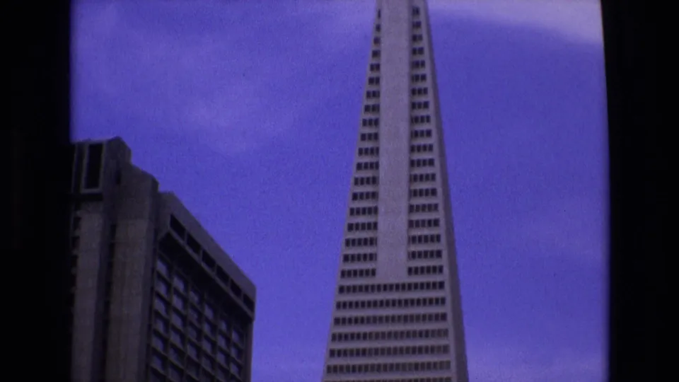 1973 San Francisco 8mm frame showing a closer low-angle view of the Transamerica Pyramid and adjacent high-rise under a purple sky.