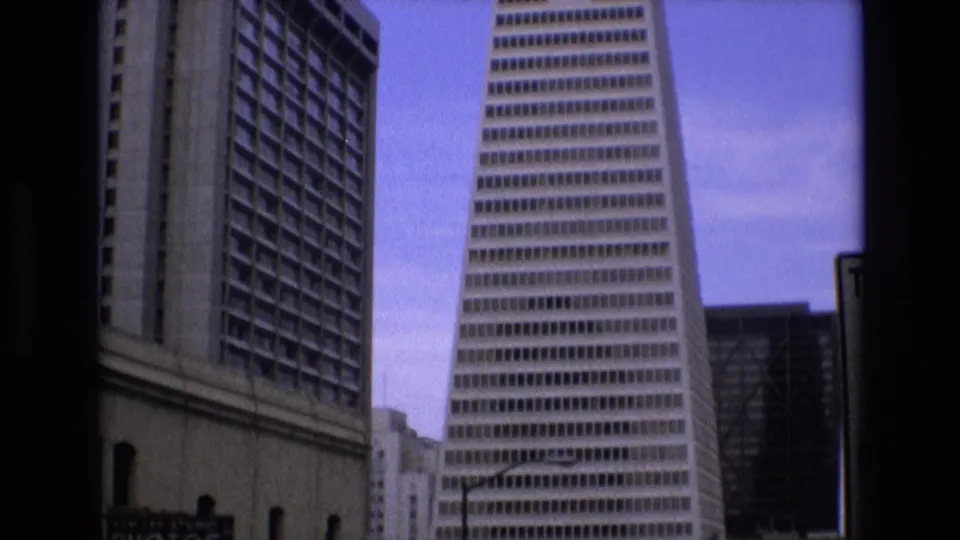 1973 San Francisco 8mm view showing the Transamerica Pyramid, an adjacent tower, visible street-level signs, and cool shifted color.