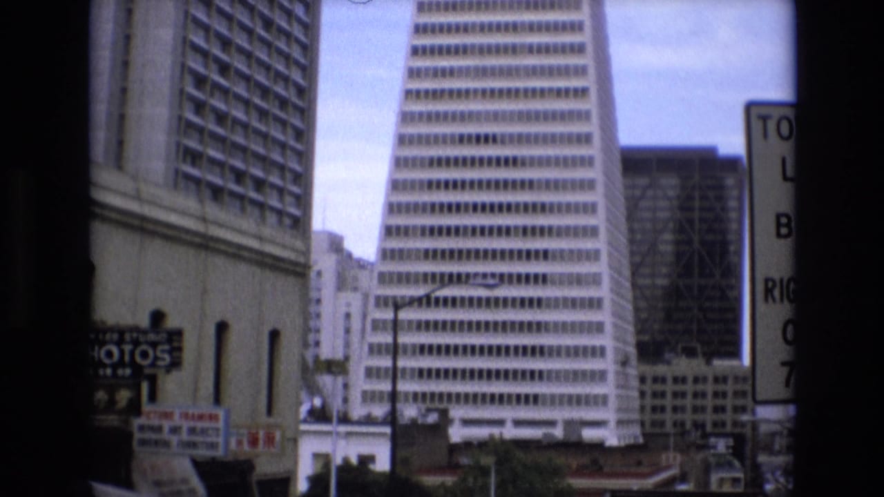 1973 San Francisco skyline view with the Transamerica Pyramid, neighboring high-rises, and partial street signage visible in a soft 8mm frame.