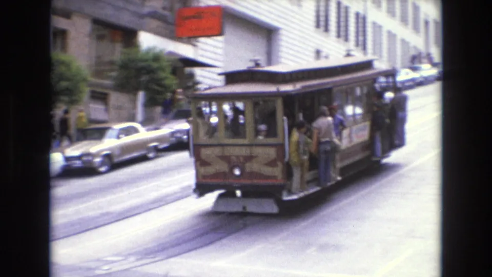 1973 San Francisco street scene showing a cable car with visible passengers, period automobiles, and buildings along a steep downtown street.