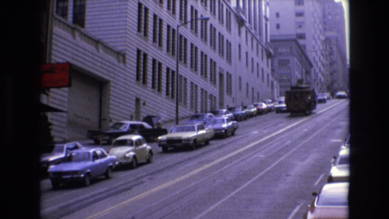 1973 San Francisco uphill street scene with a cable car near the center distance, rows of parked classic cars, and a red sign on a building.