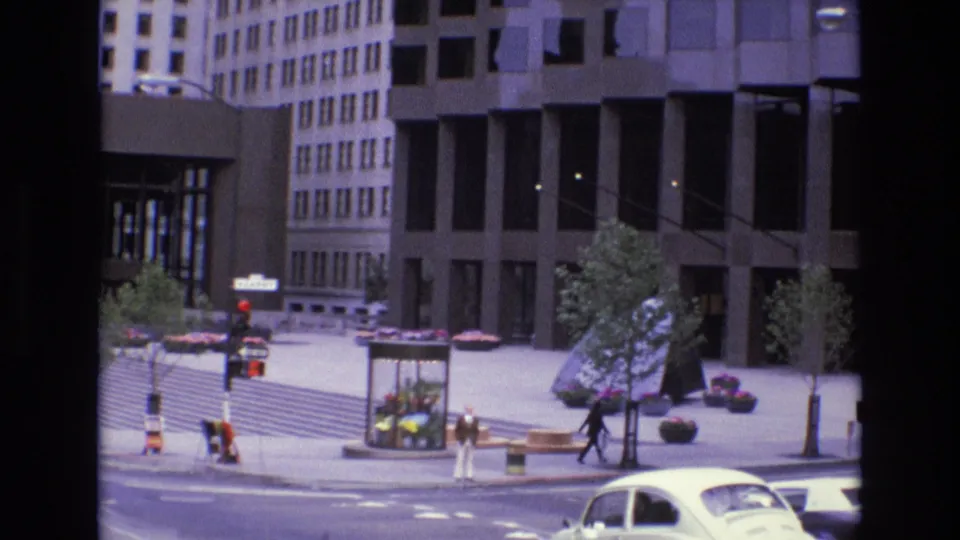 San Francisco downtown street corner in 1973 with pedestrians, a white car, planters, benches, and tall office buildings seen from an elevated home-movie viewpoint.
