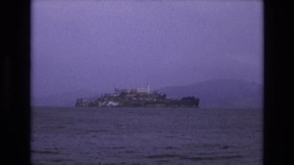 Final 1973 8mm frame of Alcatraz Island across San Francisco Bay, with visible grain, purple color shift, and dark reel borders.