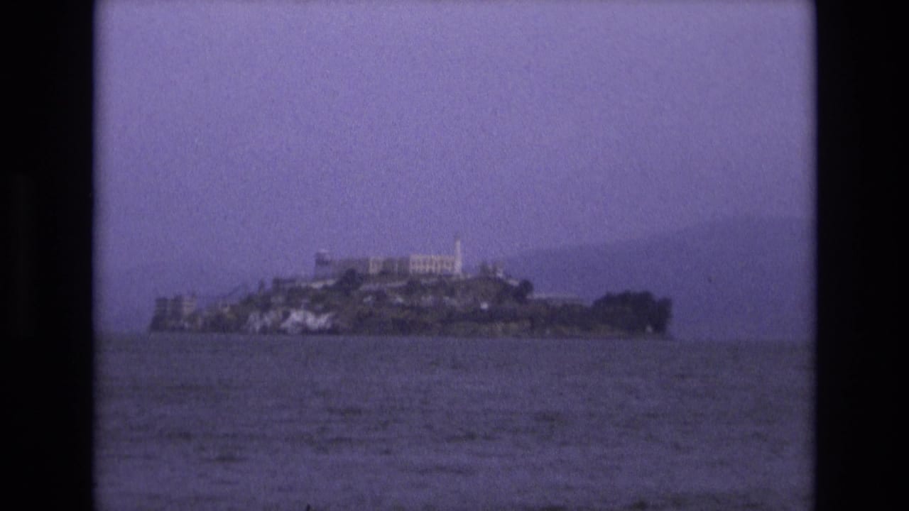 Distant Alcatraz Island across bay water under a dark hazy sky.
