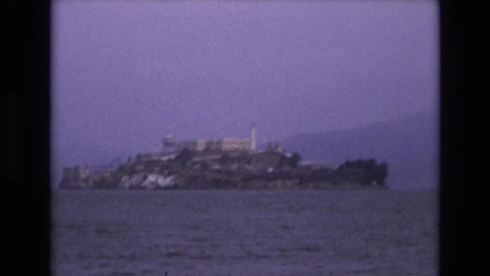 Soft 8mm frame of Alcatraz Island in San Francisco Bay, showing the island's buildings, shoreline, and surrounding water beneath a muted sky.