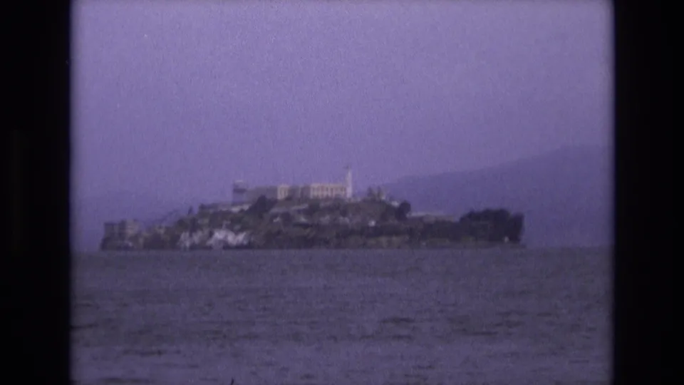 Final 1973 8mm view of Alcatraz Island from across San Francisco Bay, with rippled water, island buildings, and hazy background hills.