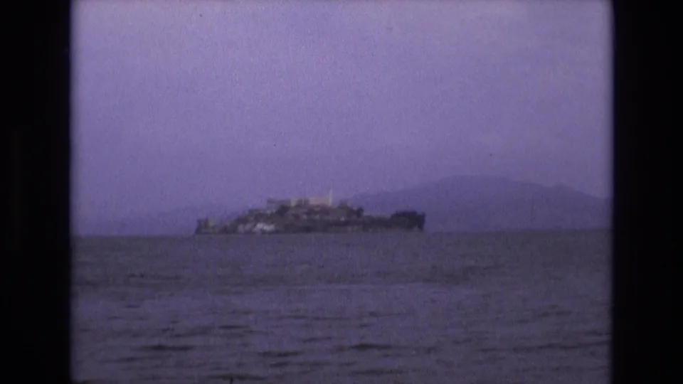 Final 1973 8mm frame of Alcatraz Island seen farther across San Francisco Bay, with low contrast, grain, and muted purple-blue color.