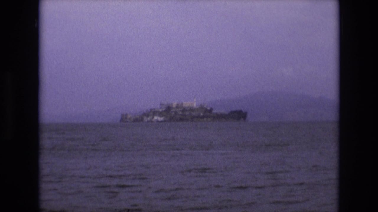 Distant view of Alcatraz Island across San Francisco Bay in 1973 8mm home-movie footage, with soft grain, purple tint, and open water in the foreground.