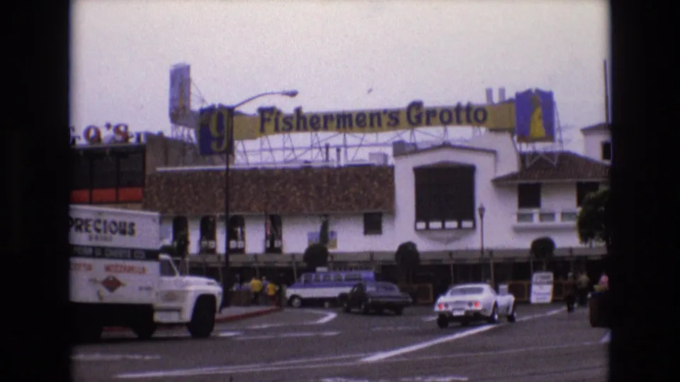 1973 San Francisco street frame outside Fisherman's Grotto, with a delivery truck entering the foreground, cars on the road, pedestrians near the building, and the large sign above the facade.