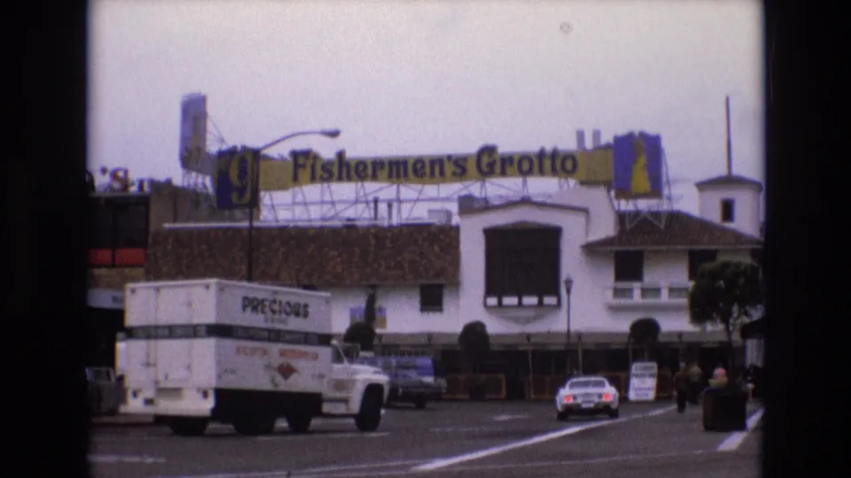 Fisherman's Grotto street view in 1973 San Francisco, with a white delivery truck in the foreground, a white car farther down the lane, pedestrians, and the restaurant sign spanning the roofline.