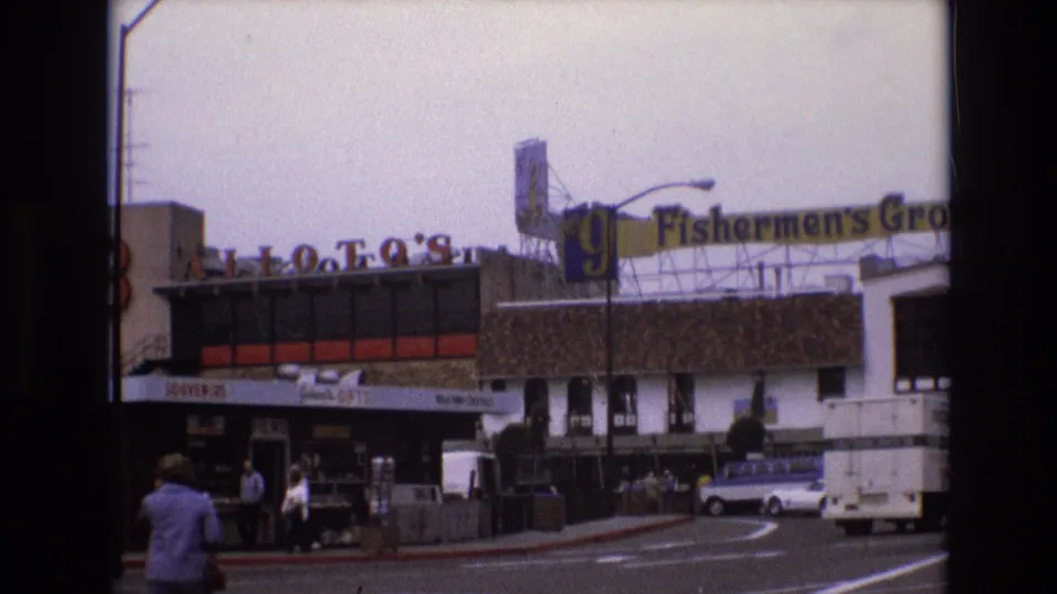 1973 San Francisco home-movie view of Fishermen's Grotto and neighboring storefronts with pedestrians on the sidewalk and period cars along the street.