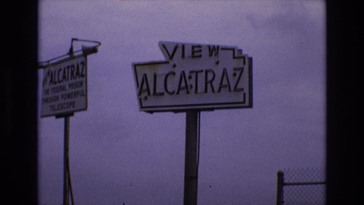 Alcatraz viewing sign beside a smaller telescope advertisement sign under a muted sky.
