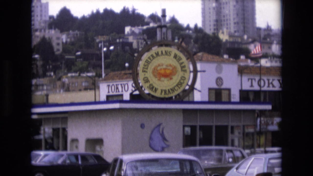 Fisherman's Wharf crab sign above a restaurant frontage with parked cars in the foreground.