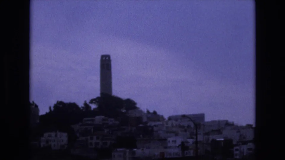 Soft 1973 8mm view of Coit Tower above San Francisco hillside residences, with visible grain, muted exposure, and dark frame edges.