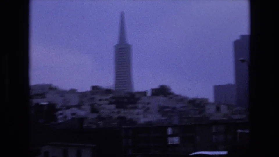 1973 8mm frame showing the Transamerica Pyramid and nearby San Francisco buildings in a soft, blue-purple skyline view.