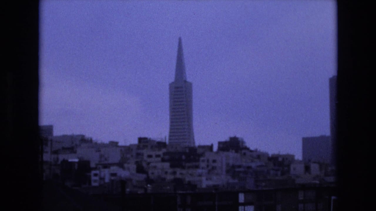 Transamerica Pyramid in the distance above clustered city buildings with dark vertical framing at the edge.