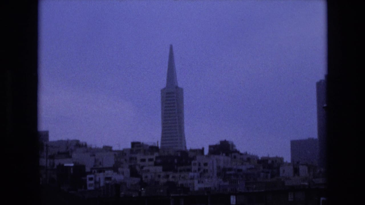 San Francisco skyline in 1973 with the Transamerica Pyramid centered beyond waterfront buildings, framed by dark vertical edges and soft 8mm grain.