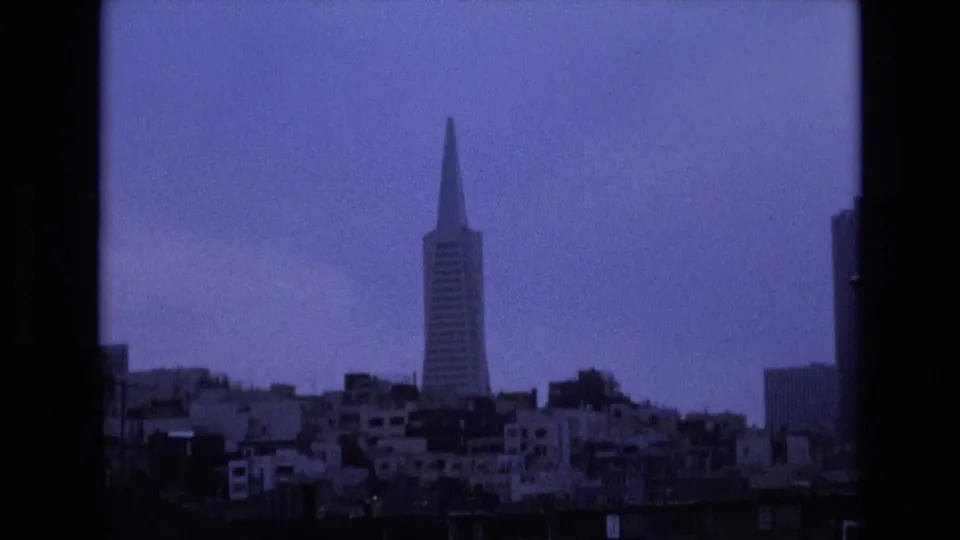 San Francisco skyline in 1973 with the Transamerica Pyramid centered beyond waterfront buildings, framed by dark vertical edges and soft 8mm grain.
