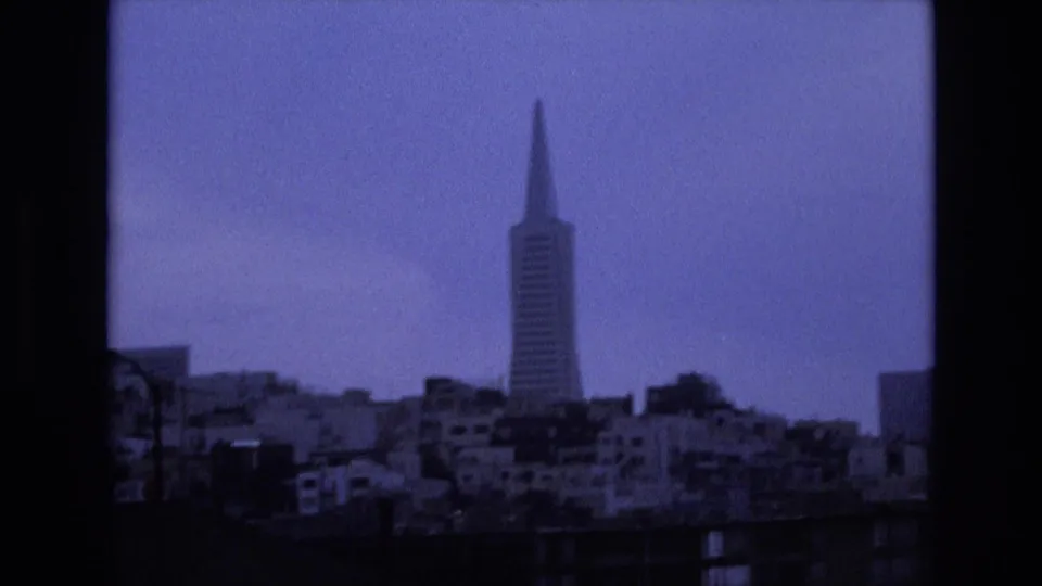 Blue-toned 8mm view of San Francisco's Transamerica Pyramid over low waterfront structures, with soft focus and visible film grain.