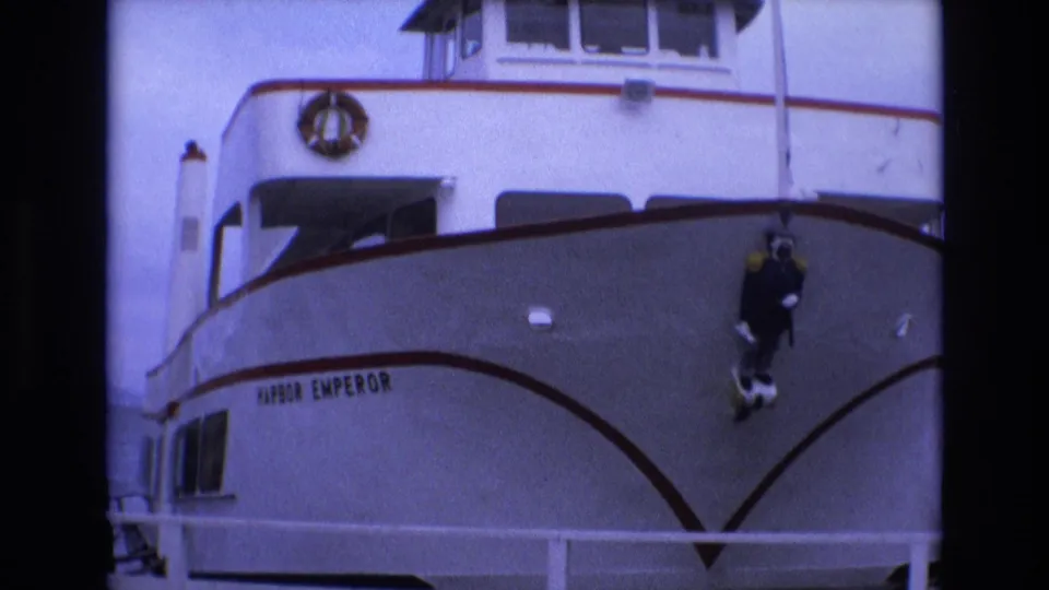 Close front view of the white ferry Harbor Emperor with red trim at the San Francisco waterfront, showing its bow, cabin windows, railings, and visible vessel name.
