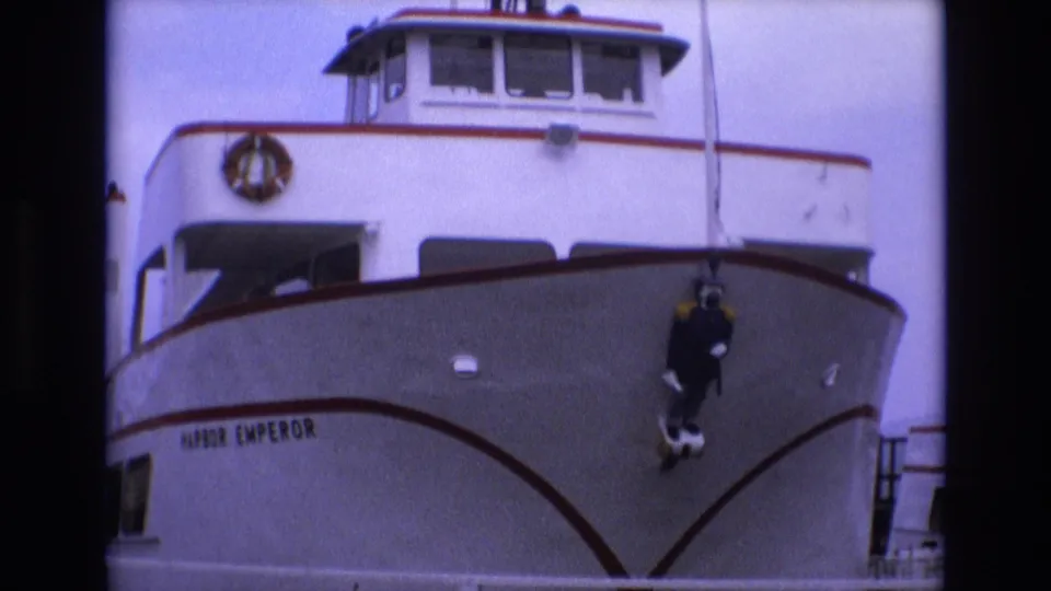 1973 San Francisco 8mm frame with the Harbor Emperor name visible on the bow, red trim lines, a life ring above, and a dark diver figure suspended near the front.