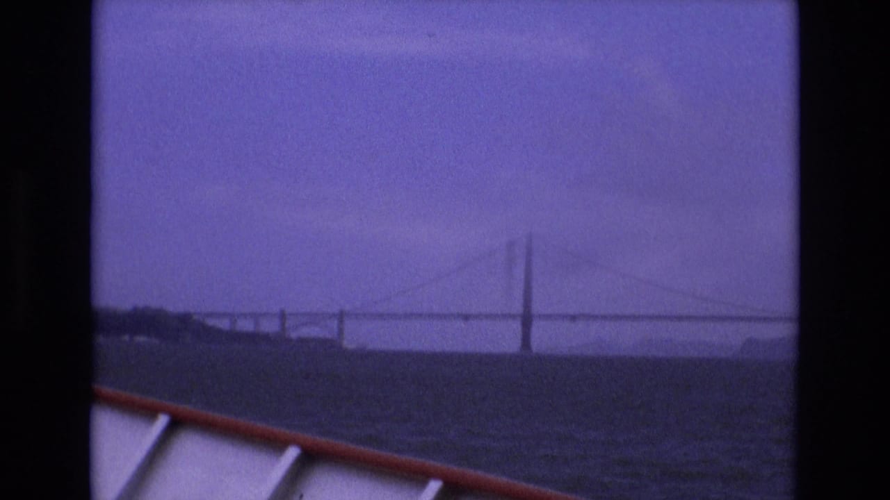1973 San Francisco 8mm view from a boat looking across dark bay water toward the Golden Gate Bridge under a hazy purple-blue sky.