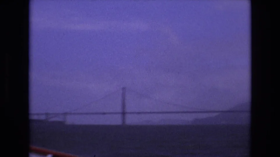 Soft 8mm frame of the Golden Gate Bridge and shoreline across San Francisco Bay, with a small section of boat railing entering the lower left corner.