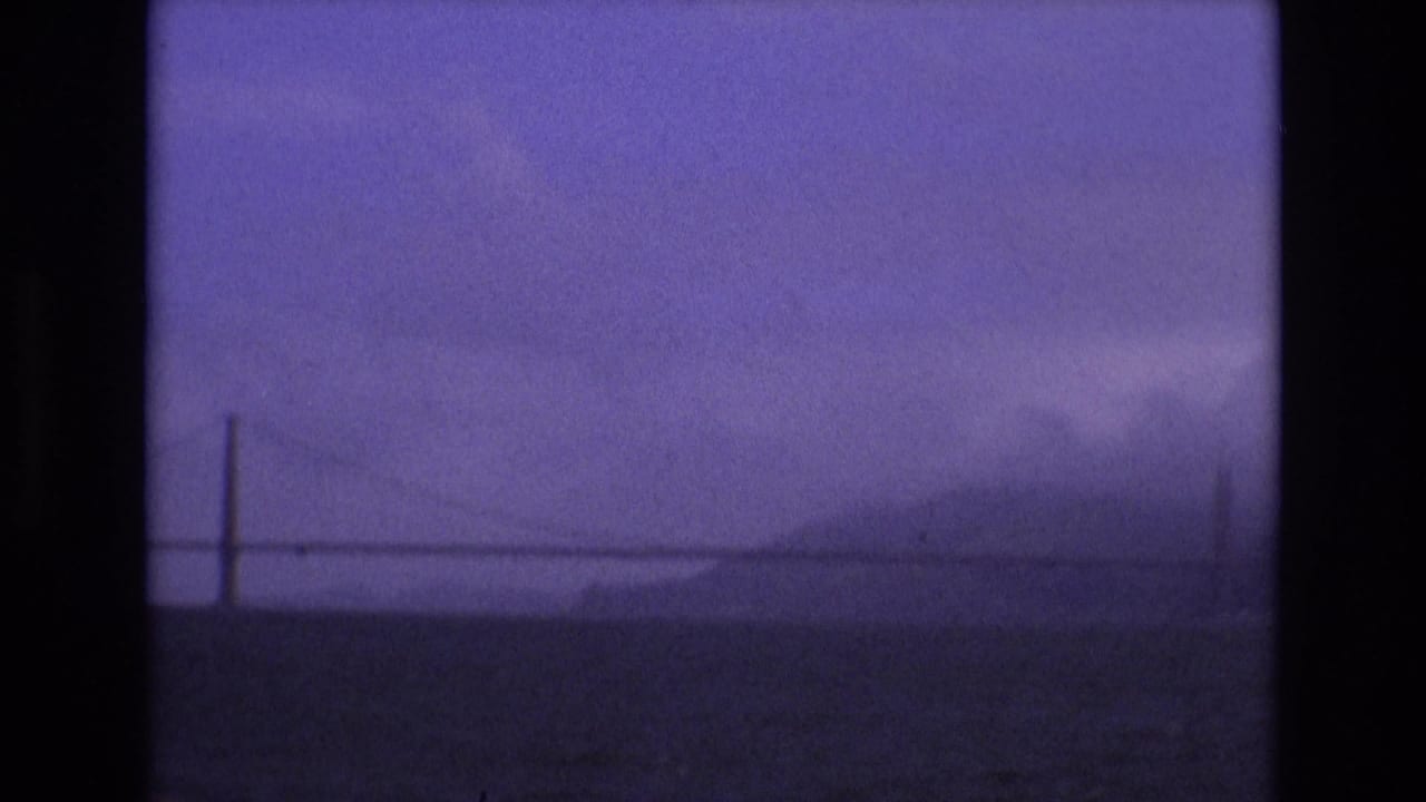 1973 San Francisco 8mm frame showing a faint Golden Gate Bridge silhouette, distant hills, fog, and dark bay water from a boat viewpoint.