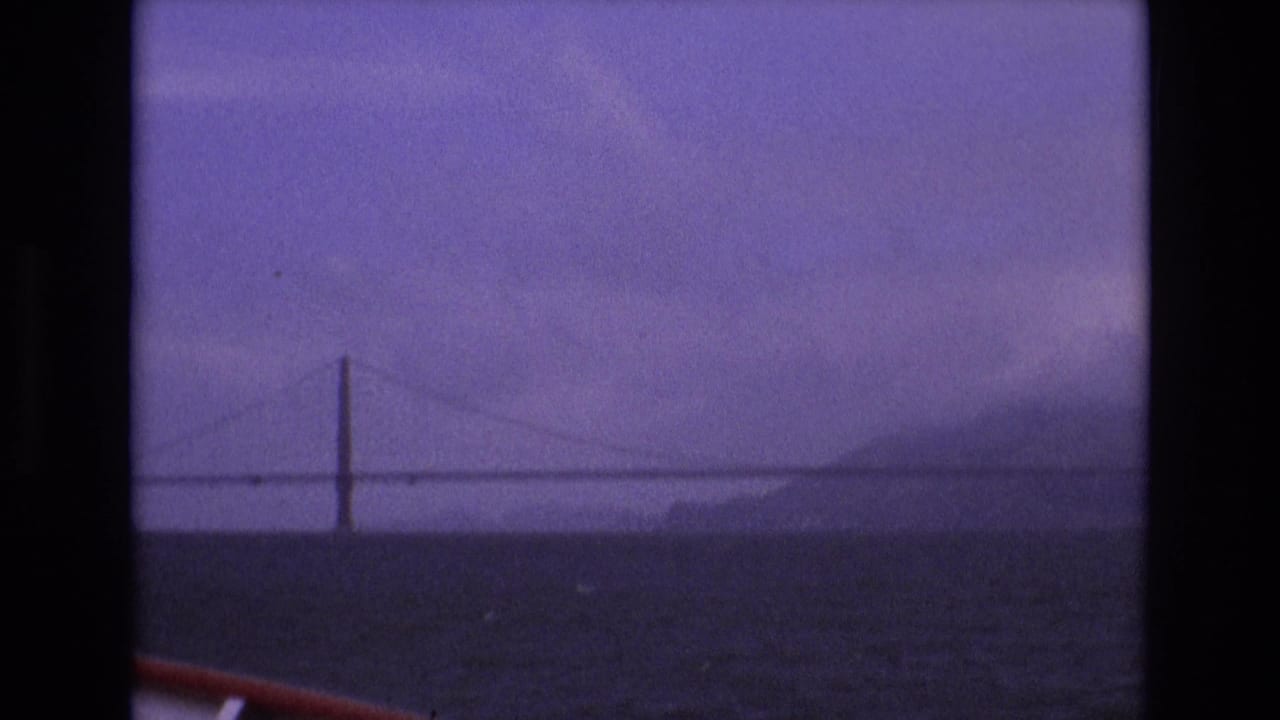 Long suspension bridge seen across dark bay water under a purple hazy sky.