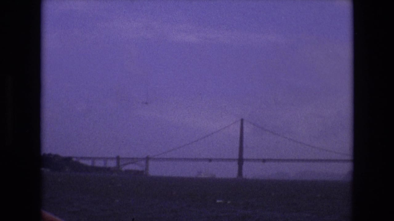 Distant suspension bridge over dark water under a hazy purple sky.