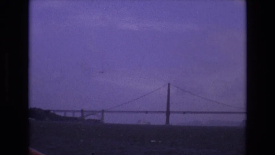 1973 8mm home-movie frame from San Francisco showing a distant suspension bridge across water beneath a purple-tinted sky.