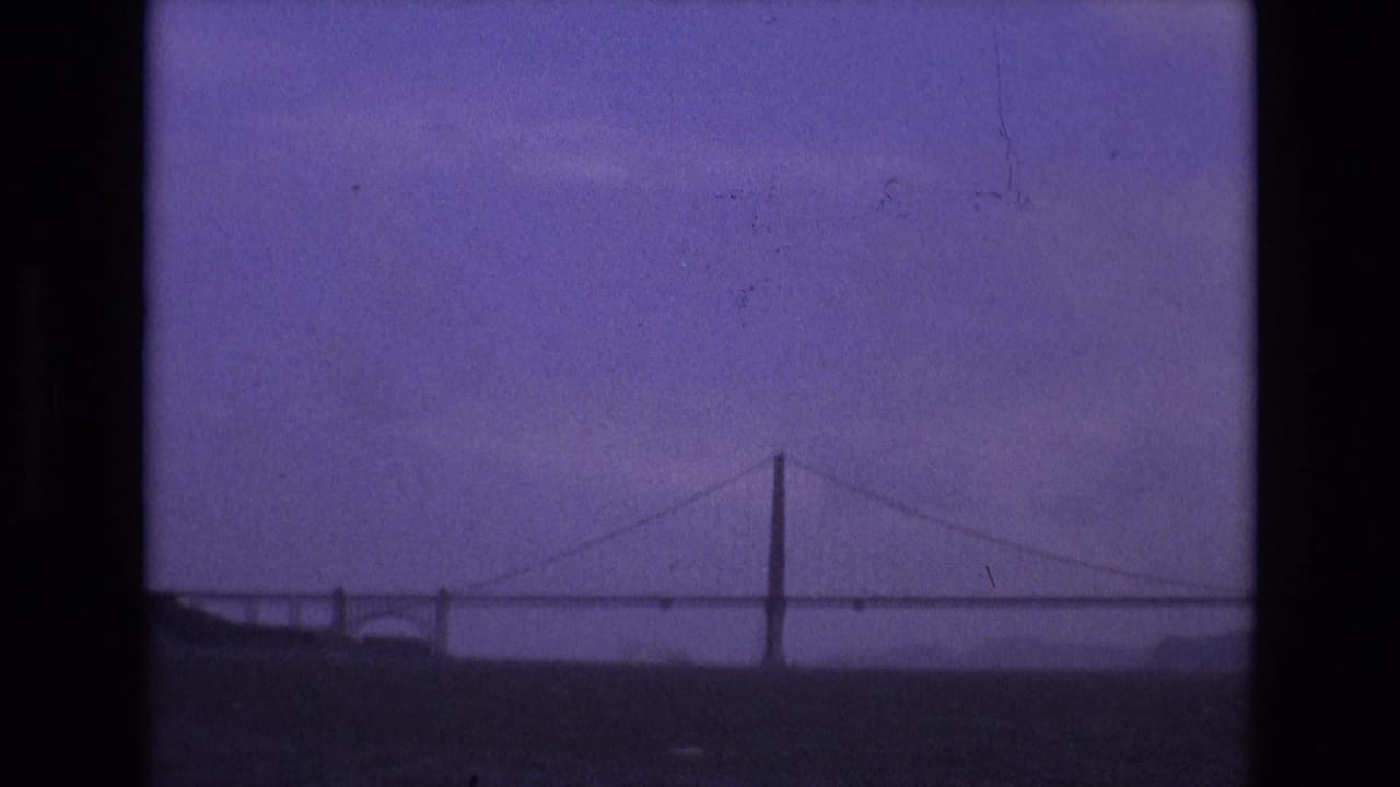 A distant suspension bridge spans the water in this purple-tinted 1973 San Francisco home-movie frame.